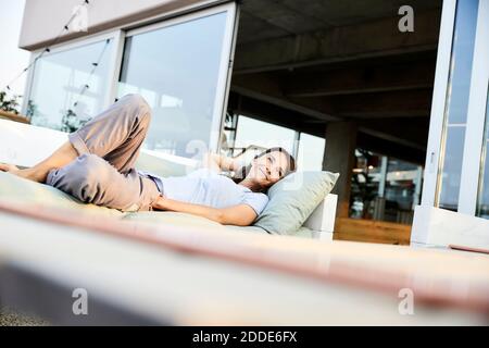 Donna sorridente che guarda via mentre si sdraiava sul divano Foto Stock