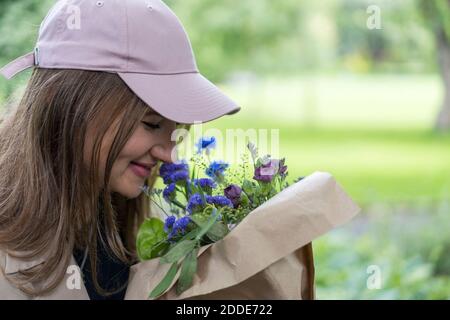 Donna sorridente che odora bouquet mentre si trova in piedi nel parco pubblico Foto Stock