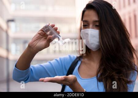 Uomo d'affari in maschera viso versando disinfettante a portata di mano durante COVID-19 Foto Stock