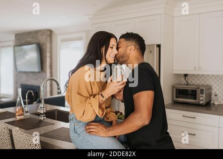 Uomo che baciava la donna seduto sul banco della cucina a casa Foto Stock