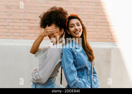 Amico che copre l'occhio con la mano mentre si sta indietro con la donna contro il muro Foto Stock
