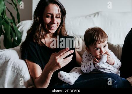 Messaggi di testo della madre sullo smartphone con il figlio seduto divano a casa Foto Stock