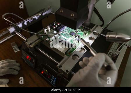 Esperto di elettronica che esamina il circuito stampato danneggiato presso l'officina di riparazione Foto Stock