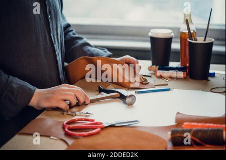 In un'officina di calzature, un tanner realizza scarpe fatte a mano utilizzando un martello e altri attrezzi. Foto Stock