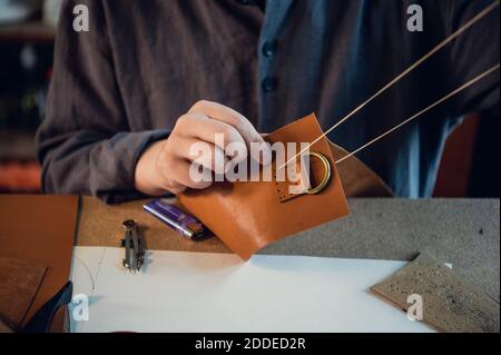 Foto ravvicinata le mani di un esperto calzolaio fanno una borsa di un pezzo di vera pelle. Foto Stock