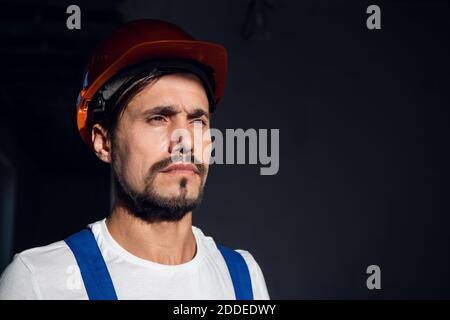 L'operaio mette un cappello arancione sulla testa. È vestito con tute e guanti. Primo piano Foto Stock