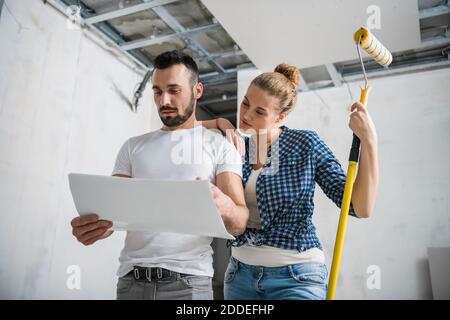 Una donna tiene un rullo in mano e abbraccia il marito. Guardano alla disposizione degli appartamenti Foto Stock