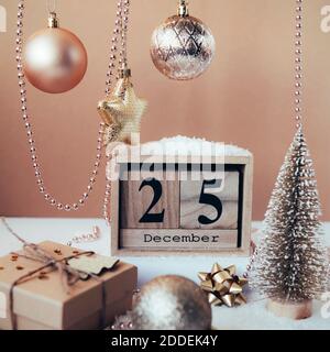 Calendario blocco di legno con data 25 dicembre, decorazioni natalizie e scatola regalo su sfondo beige. Foto Stock