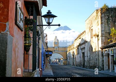 Il vulcano Agua, protetto dalle nuvole, è uno dei tre vulcani che si affacciano sulla città coloniale di Antigua, Guatemala. Vista da Calle del Arco, la Via dell'Arco, il monumento vulcanico offre uno sfondo per l'Arco di Santa Catalina, un monumento storico costruito nel 1694. L'arco, storicamente, ha collegato due conventi, Convento della Vergine e Convento di Santa Catalina. Le monache erano tenute a non essere viste in pubblico così l'arco ha una passerella segreta affinchè loro attraversi fra i due conventi. L'orologio all'aperto in stile francese sull'arco è stato aggiunto nel 1800 e deve essere avvolto ogni tre giorni. Foto Stock