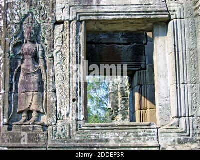 Un intricato bassorilievo di un'apsara cambogiana scolpita in un muro nel Bayon di Angkor Thom. Attraverso lo spazio aperto si può vedere una delle molte grandi facce di pietra che sono scolpite in torri di granito in tutto il prasat bayon. Parte delle meraviglie architettoniche Khmer in tutta l'area di Siem Reap, Cambogia, Angkor Thom insieme ad Angkor Wat attraggono milioni di turisti in queste città perdute che sono ancora in via di scavo e conservazione. Foto Stock