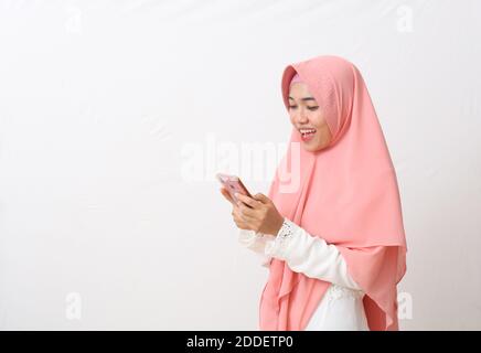 Un ritratto della donna musulmana asiatica felice che indossa un velo o un hijab usando un telefono cellulare e sorridendo. Ricevere buone notizie, concetto di comunicazione moderna. ISOL Foto Stock