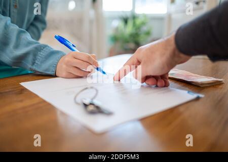 Un riattore punta al contratto per la firma. Primo piano delle mani. Sul tavolo sono presenti dei tasti. Affitto e acquisto di immobili. Foto Stock