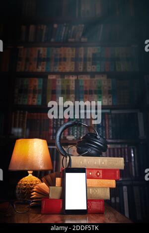 Telefono cellulare raggruppato, cuffie e una pila di libri vicino alla lampada su un tavolo di legno. Concetto di formazione e audiolibri. Libreria libreria nel bac Foto Stock