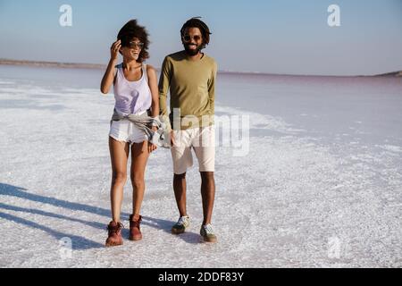 Giovane coppia africana che ama camminare lungo la riva del mare, tenendo le mani Foto Stock