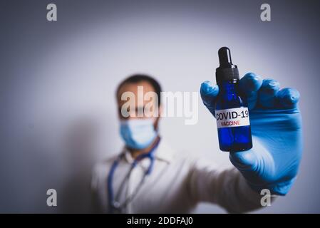 giovane medico di sesso maschile che contiene cocid19 siringa di vaccino. concetto di scienza e vaccino del coronavirus. maschera facciale e stetoscopio sfondo bianco, atmosfera scura Foto Stock