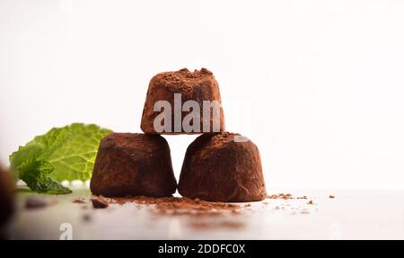 Tartufi di cioccolato con cacao in polvere su banco da cucina e foglie di menta. Vista frontale. Composizione orizzontale. Foto Stock