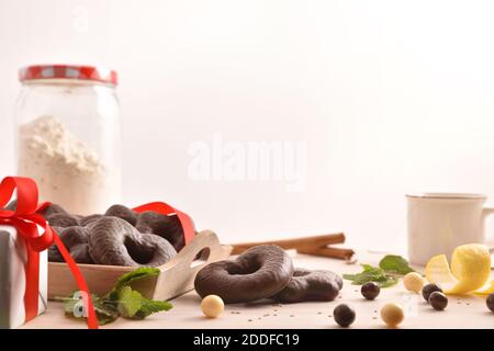 Biscotti di cioccolato a forma di cuore e stella su vassoio e menta, bastoncini di cannella e limone su tavolo di legno con regali e tazza di infusione sfondo isolato. Fro Foto Stock