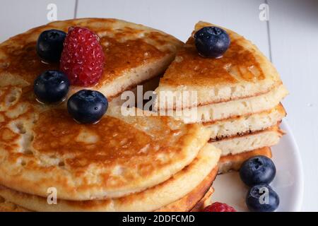 Piatto di frittelle tagliate a triangolo con sciroppo d'acero, mirtilli e lamponi su tavolo di legno bianco e vista dall'alto. Foto Stock