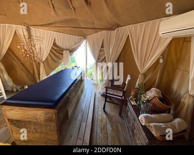 Comodo letto di massaggio blu in tenda estiva beige con tende bianche e vista mare all'aperto. Relax esotico vacanza estiva di lusso terapia all'aperto. Foto Stock
