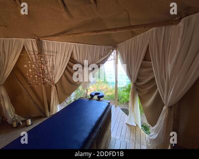 Comodo letto di massaggio blu in tenda estiva beige con tende bianche e vista mare all'aperto. Relax esotico vacanza estiva di lusso terapia all'aperto. Foto Stock