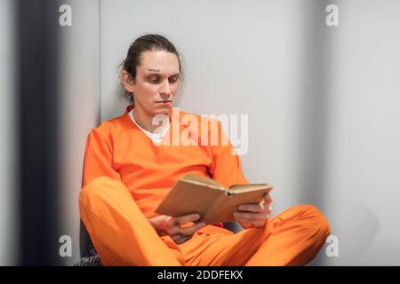 Un giovane compagno con un volto tatuato viene addestrato a distanza in una cella. Legge un libro di testo seduto su una cuccetta Foto Stock