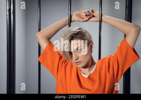 Un ritratto ravvicinato di un detenuto in prigione con ruggito arancione sullo sfondo di bar carcerari. Foto Stock