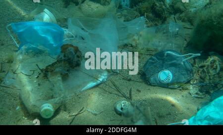 Morto più grande pesce di svezzamento (Trachinus draco) colpire intrappolato in sacchetto di plastica si trova all'interno del sacchetto di plastica sul fondo marino tra la maschera medica viso, plastica A. Foto Stock