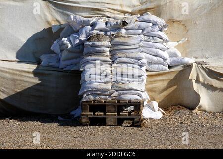 Sacchi di sabbia bianchi nuovi e vecchi, parzialmente rotti, utilizzati per l'alluvione protezione su pallet in legno accanto alla protezione temporanea contro le alluvioni parete Foto Stock
