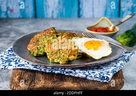 Frittelle di zucchine e piselli verdi con uova fritte e pomodoro salsa - cibo vegetariano sano Foto Stock