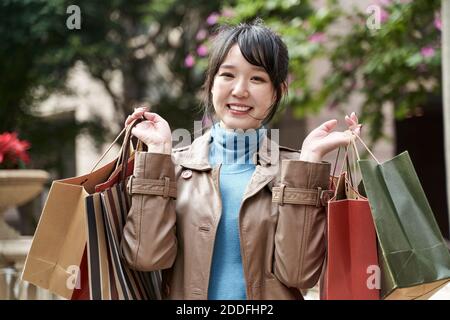 bello felice giovane asiatico portare borse per lo shopping guardando la macchina fotografica sorridente Foto Stock