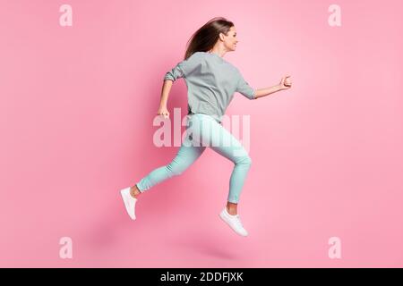 Foto profilo a dimensione intera di dolce capelli lunghi ragazza salto run mani pugni indossare camicia blu pantaloni sneakers bianco isolato su sfondo rosa Foto Stock