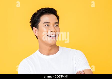 Primo piano ritratto di giovane bell'uomo asiatico allegro sorridente e guardando via in studio isolato sfondo giallo Foto Stock