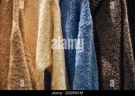 Pullover invernali lavorato a maglia su una rastrelliera in un negozio di moda. Immagine concettuale di Capsule wardrobe dei pullover nel negozio di panni. Pullover caldi fatti a mano in lana. Foto Stock