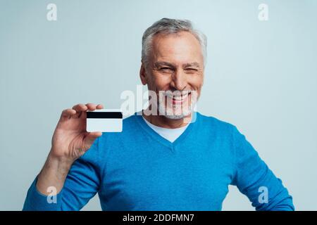 Bello senior isolato su sfondo grigio. Vecchio uomo che fa shopping in linea. Concetto circa la terza età e anzianità Foto Stock