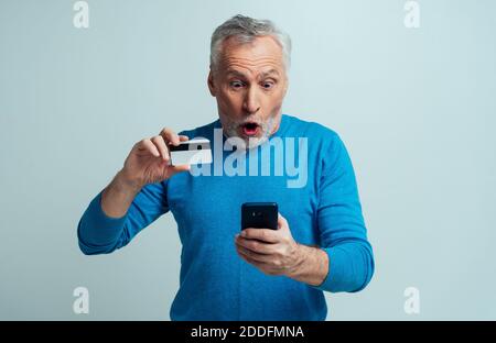 Bello senior isolato su sfondo grigio. Vecchio uomo che fa shopping in linea. Concetto circa la terza età e anzianità Foto Stock