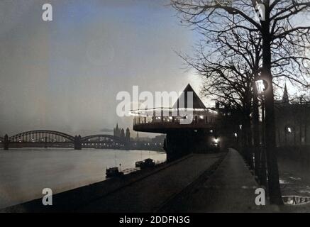 Blick auf die Bastel, die Hohenzollernbrücke und die Altstadt mit der Kirche Groß San Martin am Rheinufer bei Nacht in Köln, Deutschland 1920er Jahre. Vista al ristorante Bastei, Hohenzollernbruecke bridge, la città vecchia con Gross la chiesa di San Martino con il fiume Reno a Colonia, Germania 1920s. Foto Stock