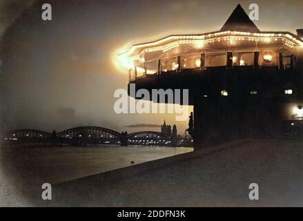 Blick auf die Bastel, die Hohenzollernbrücke und die Altstadt mit der Kirche Groß San Martin am Rheinufer bei Nacht in Köln, Deutschland 1920er Jahre. Vista al ristorante Bastei, Hohenzollernbruecke bridge, la città vecchia con Gross la chiesa di San Martino con il fiume Reno a Colonia, Germania 1920s. Foto Stock