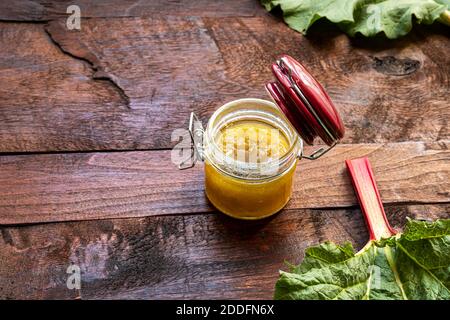 Un vaso di vetro aperto di marmellata di rabarbaro fatto in casa e fresco rabarbaro gambi organici su un vecchio tavolo di legno scuro, spazio copia Foto Stock