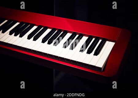 Sintetizzatore elettronico (tastiera a piano) primo piano con sfondo scuro. Bella tastiera musicale rossa con tasti balck e bianchi. Foto Stock