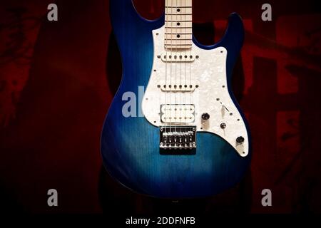 Bella, nuova, chitarra elettrica blu e bianca con sfondo rosso. Foto in primo piano minimalistica moderna con spazio per il testo. Foto Stock