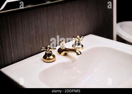 Lavabo bianco e pulito con rubinetto d'oro. Rubinetto d'epoca per il bagno, design degli interni dell'hotel. Scatti chiari e minimalisti con sfondo scuro. Foto Stock