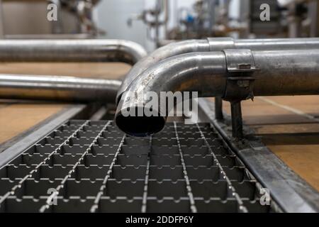 Tubo di scarico e scarico dell'acqua dall'acciaio inossidabile utilizzato nell'industria alimentare. Scarico a pavimento in primo piano nello stabilimento di produzione Foto Stock