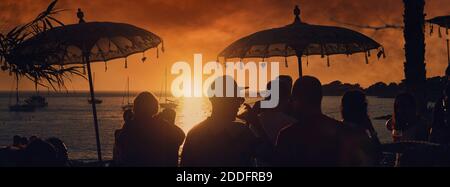 Un gruppo di persone irriconoscibili con vista panoramica si trova al bar del night club pubblico durante il luminoso tramonto arancione sul Calo des Moro di Ibiza. Viaggi, feste Foto Stock