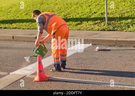 Un operaio di strada disegna una linea di arresto sull'asfalto con vernice bianca usando una lattina di irrigazione - Mosca, Russia, 18 giugno 2020 Foto Stock
