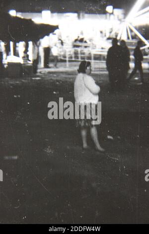 Bella fotografia in bianco e nero degli anni '70 di una donna in attesa di qualcuno al carnevale locale in serata. Foto Stock