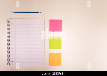 Blocco note, matita e piccola nota colorata su una scrivania bianca Foto Stock