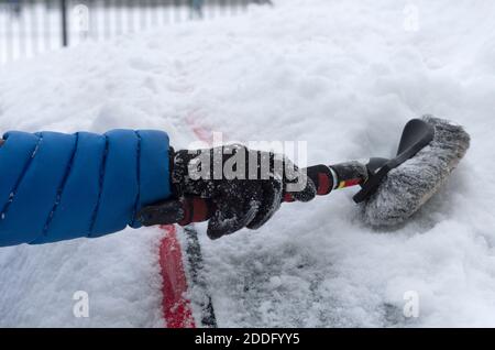 La mano dell'uomo con una spazzola pulisce l'auto da un molta neve da vicino Foto Stock