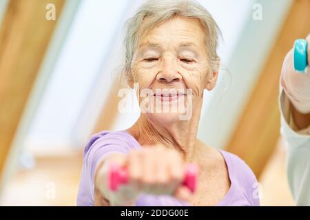 Donna anziana come un manubri sollevamento manubri durante la riabilitazione in fisioterapia Foto Stock
