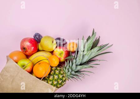 Frutti tropicali. Ananas. Cocco, arancio, banane in borsa carta su sfondo rosa. Concetto di cibo. Composizione tropicale estiva. Vista dall'alto, co Foto Stock