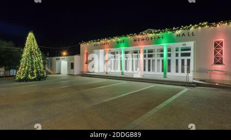 La War Memorial Hall di Katikati, Nuova Zelanda, si è illuminata di notte con luci di Natale verdi e rosse. Un albero di Natale si erge nella piazza davanti Foto Stock